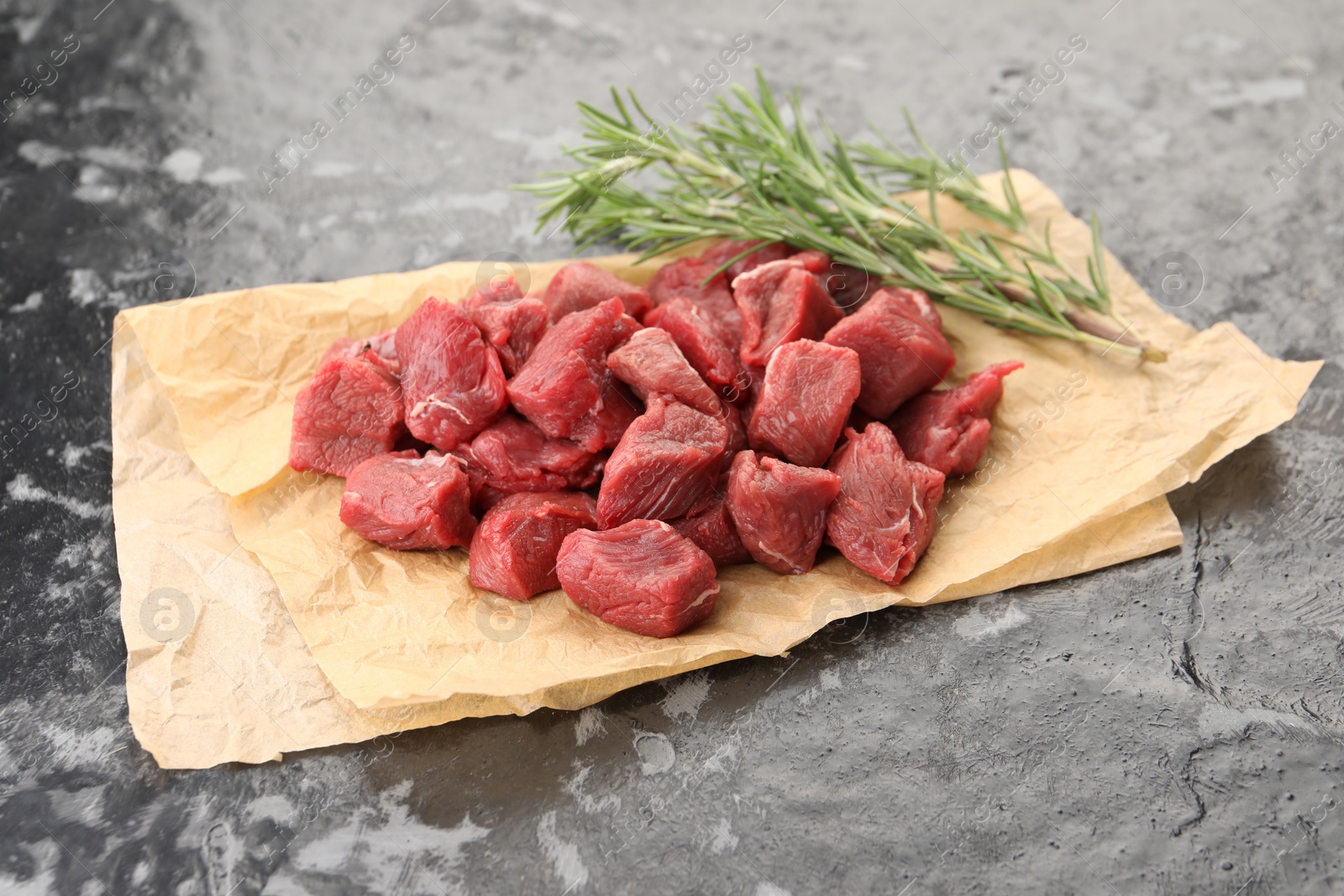 Photo of Pieces of raw beef meat and rosemary on grey textured table