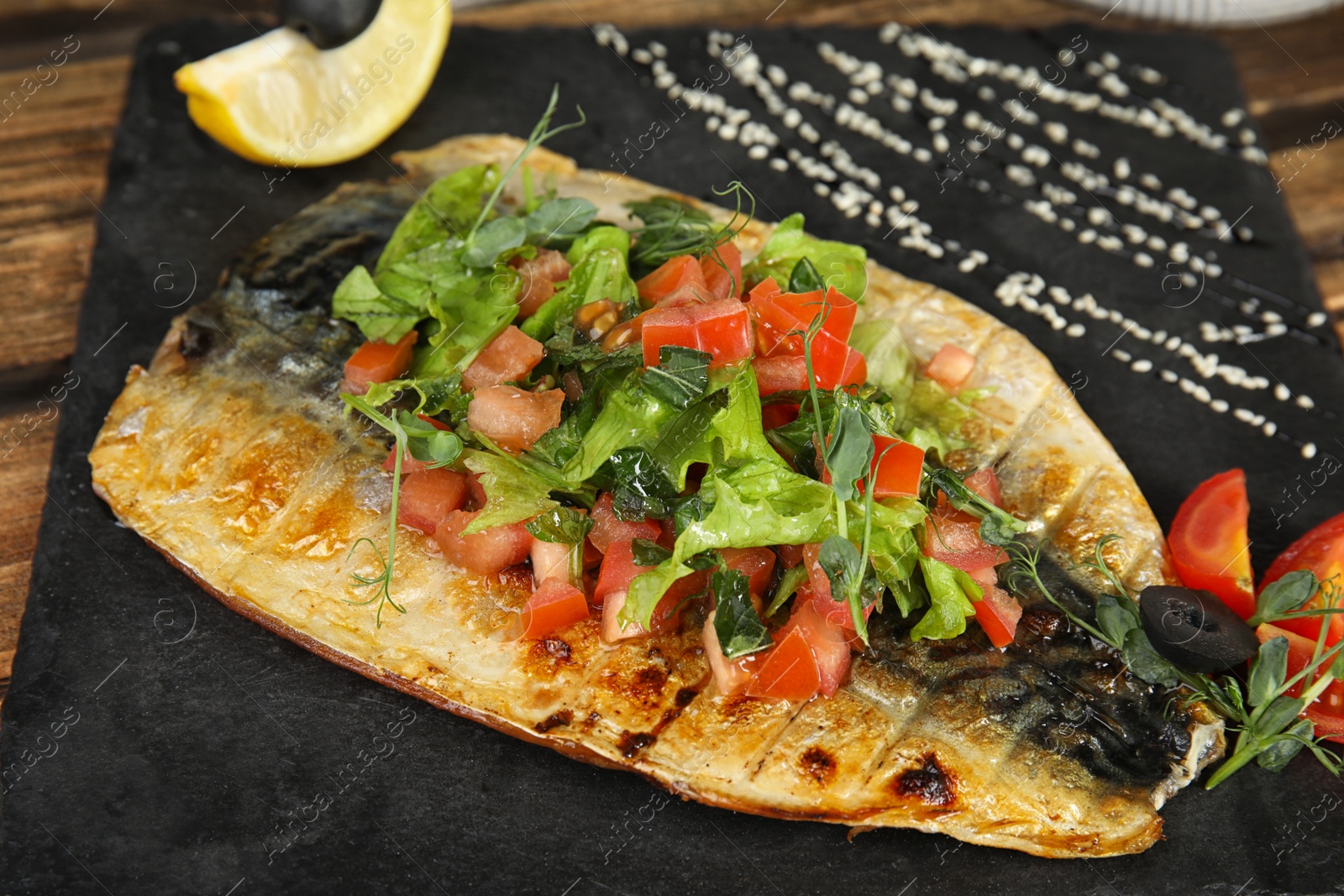 Photo of Delicious grilled fish with vegetables on slate plate, closeup