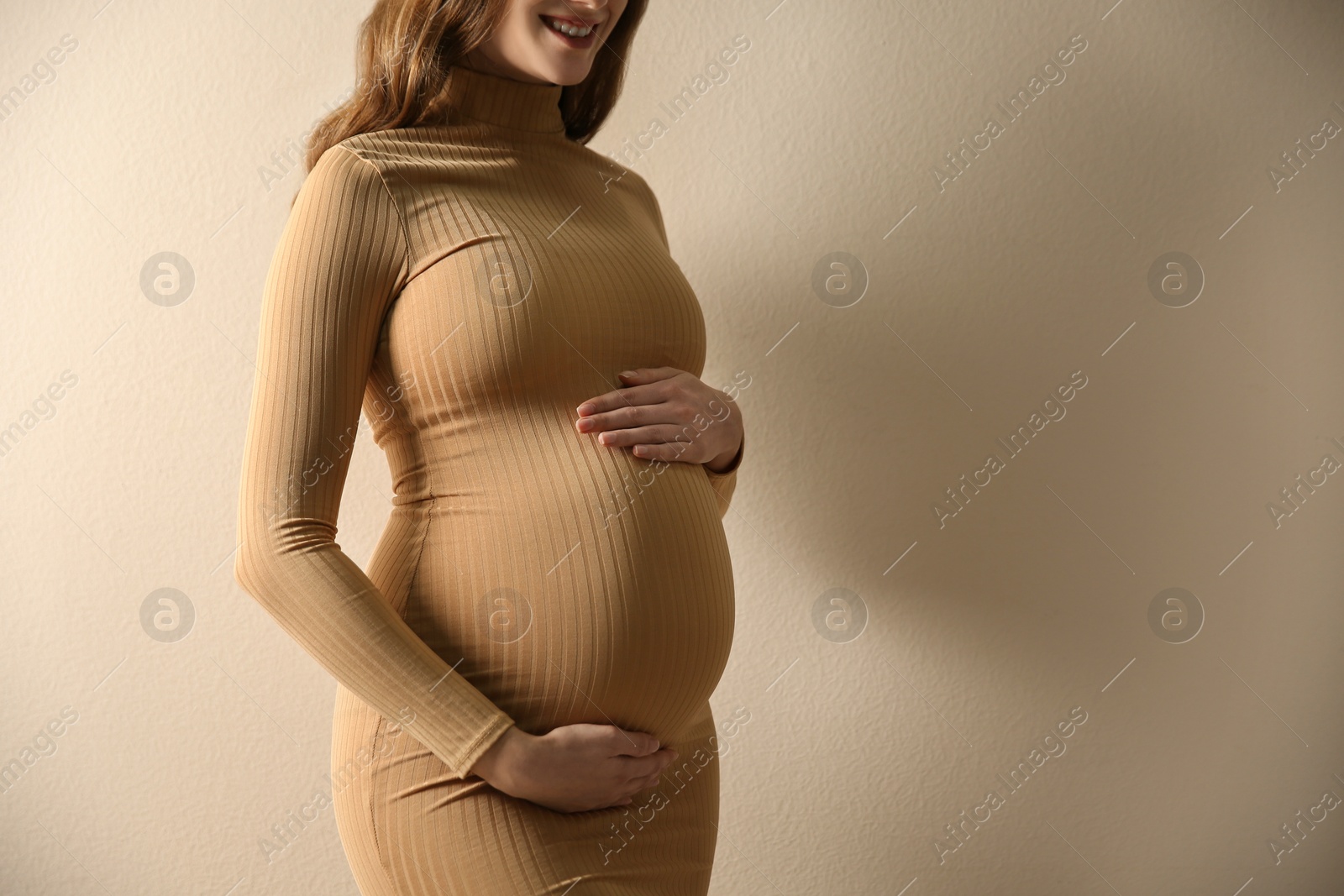 Photo of Pregnant woman touching her belly on beige background, closeup. Space for text