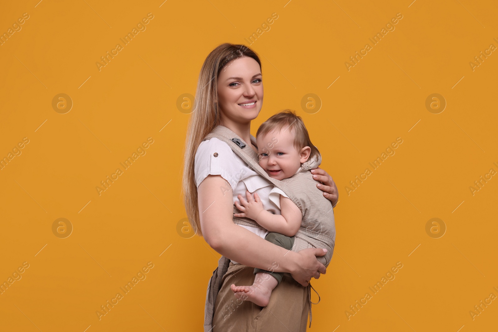 Photo of Mother holding her child in sling (baby carrier) on orange background. Space for text