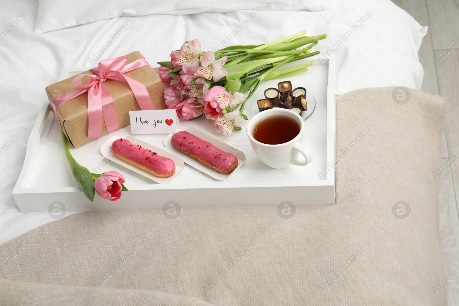 Photo of Tasty breakfast served in bed. Delicious desserts, tea, flowers, gift box and card with phrase I Love You on tray