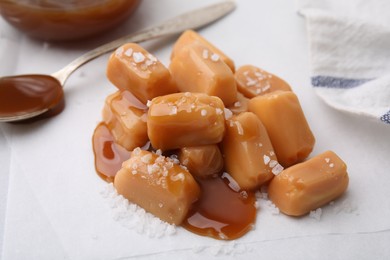 Photo of Yummy caramel candies and sea salt on white table, closeup