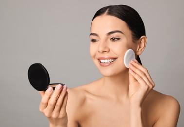 Photo of Beautiful young woman applying face powder with puff applicator on grey background