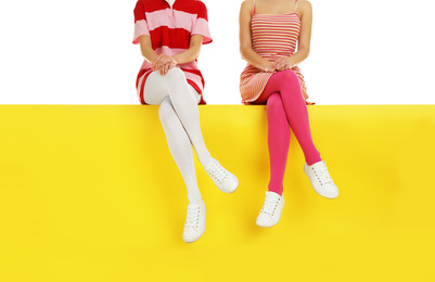 Women wearing bright tights sitting on color background, closeup