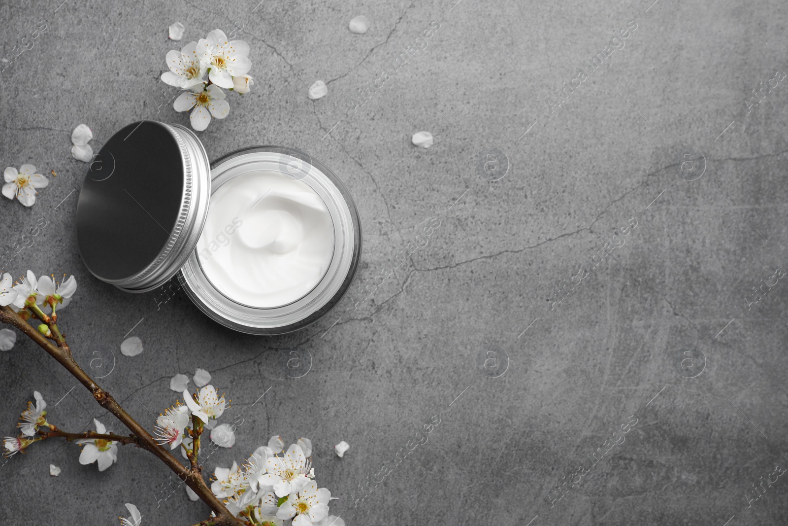 Photo of Flat lay composition with jar of face cream and flowers on grey table. Space for text