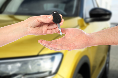 Car buying. Woman giving key to new owner against blurred automobile, closeup