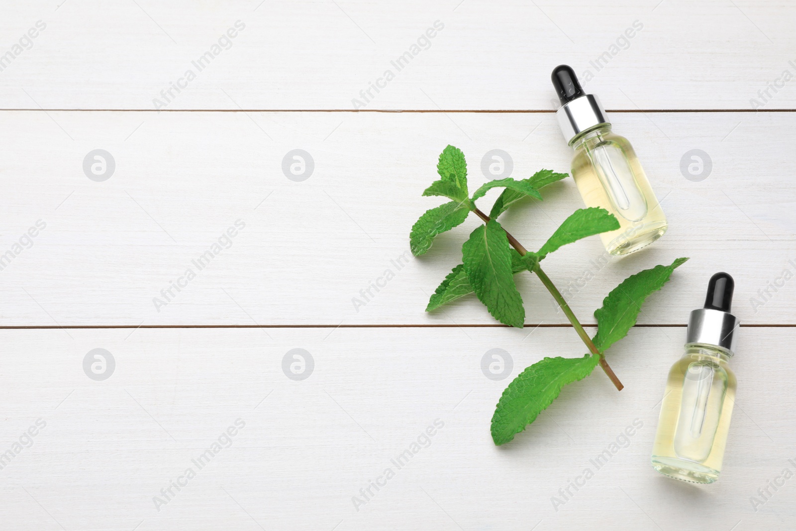 Photo of Bottles of essential oil and mint on white wooden table, flat lay. Space for text