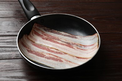 Photo of Slices of raw bacon in frying pan on wooden table, closeup