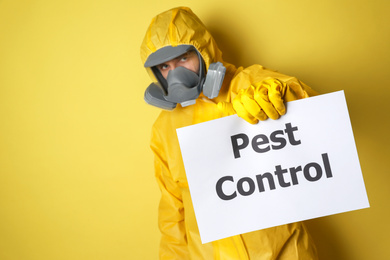 Photo of Man wearing protective suit with insecticide sprayer holding sign PEST CONTROL on yellow background