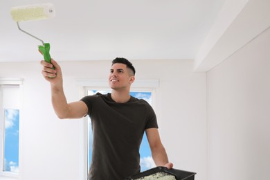 Man painting ceiling with roller in room. Space for text