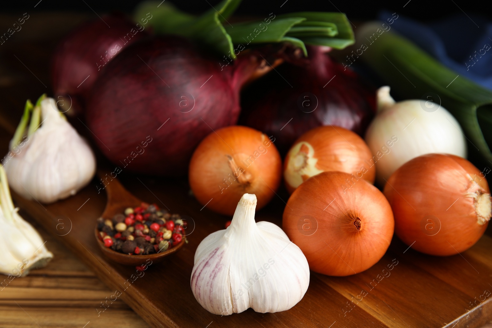 Photo of Fresh onion bulbs, leek, garlic and peppers mix on wooden table, closeup