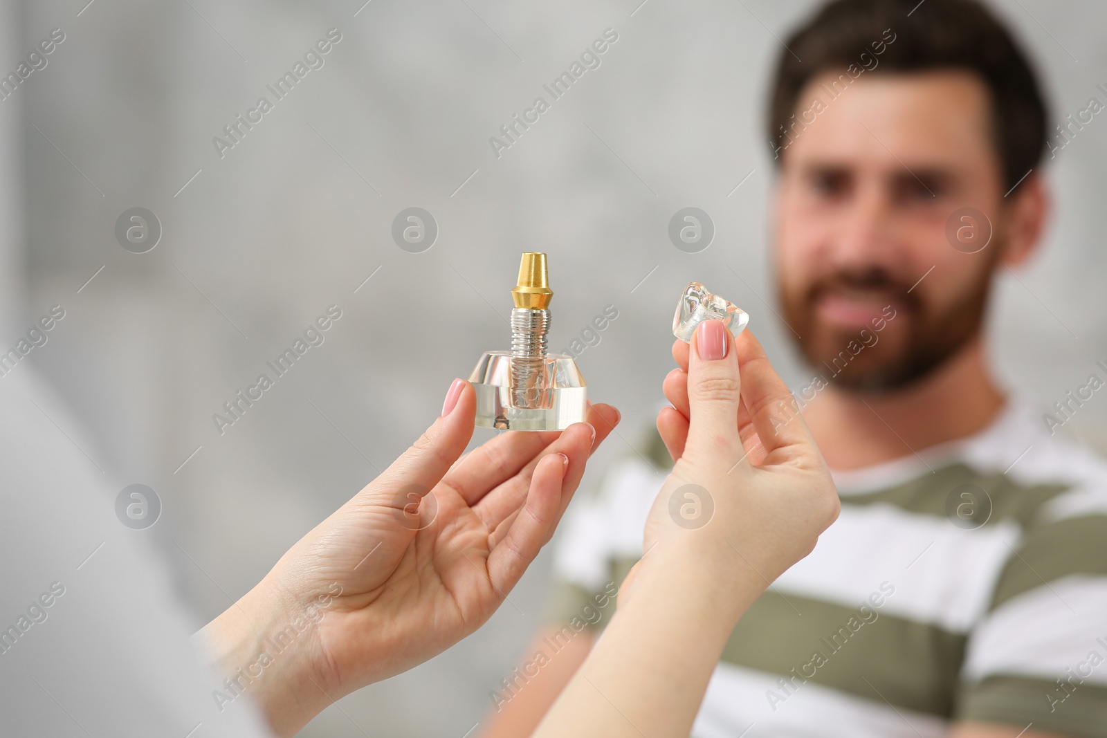 Photo of Doctor with educational model of dental implant consulting patient in clinic, closeup