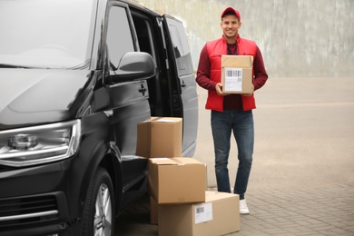 Photo of Courier with parcels near delivery van outdoors