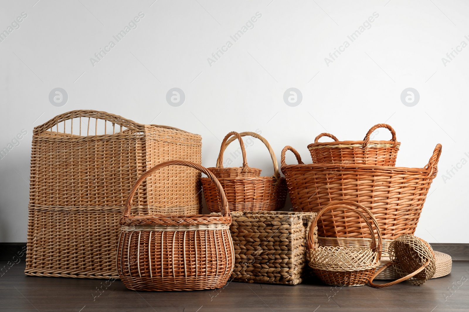 Photo of Many different wicker baskets made of natural material on floor near light wall