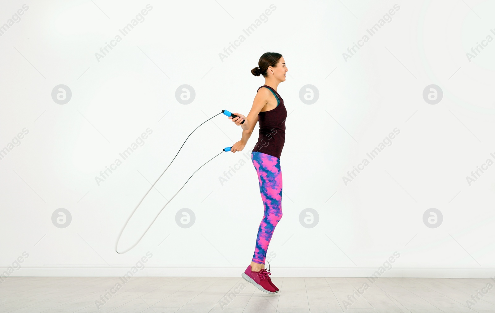 Photo of Young sportive woman training with jump rope in light room