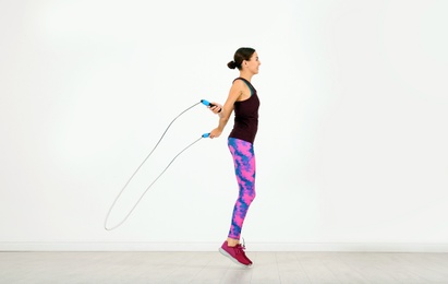 Young sportive woman training with jump rope in light room