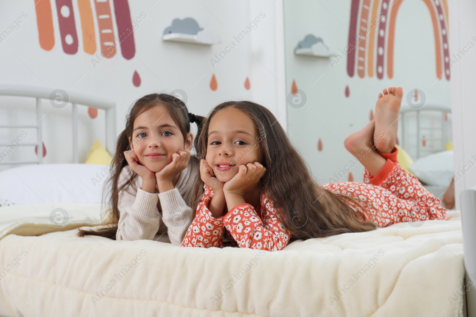 Photo of Cute girls in pajamas on bed at home