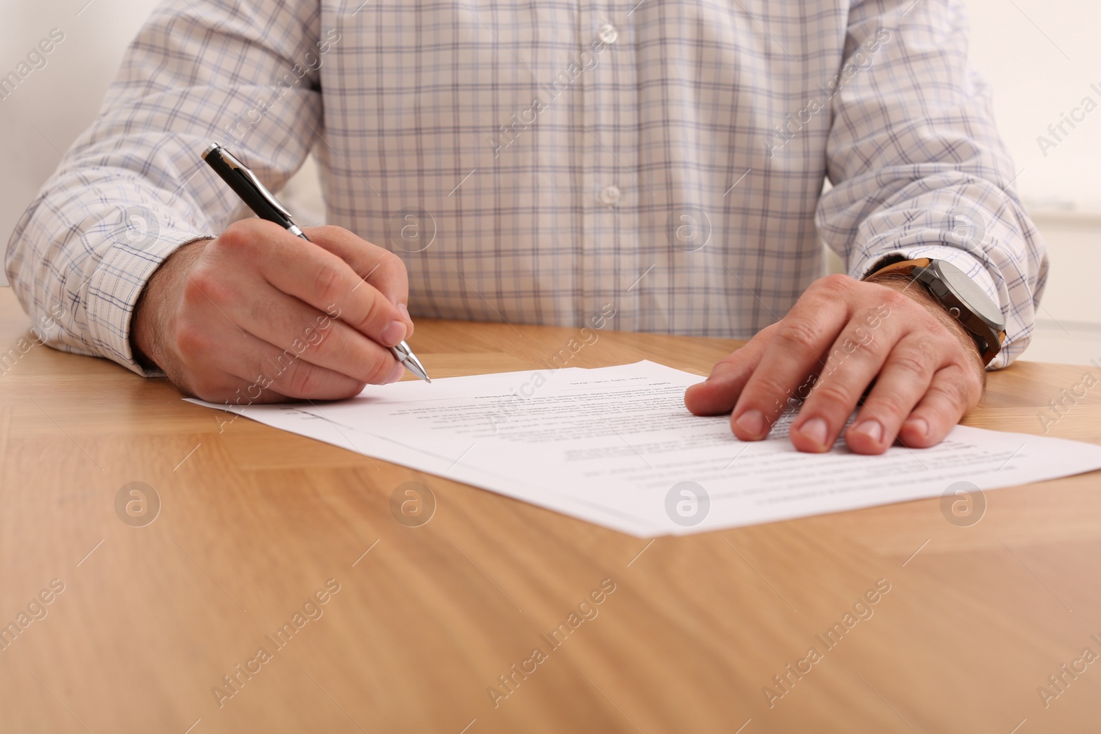 Photo of Businessman signing contract at wooden table, closeup of hands