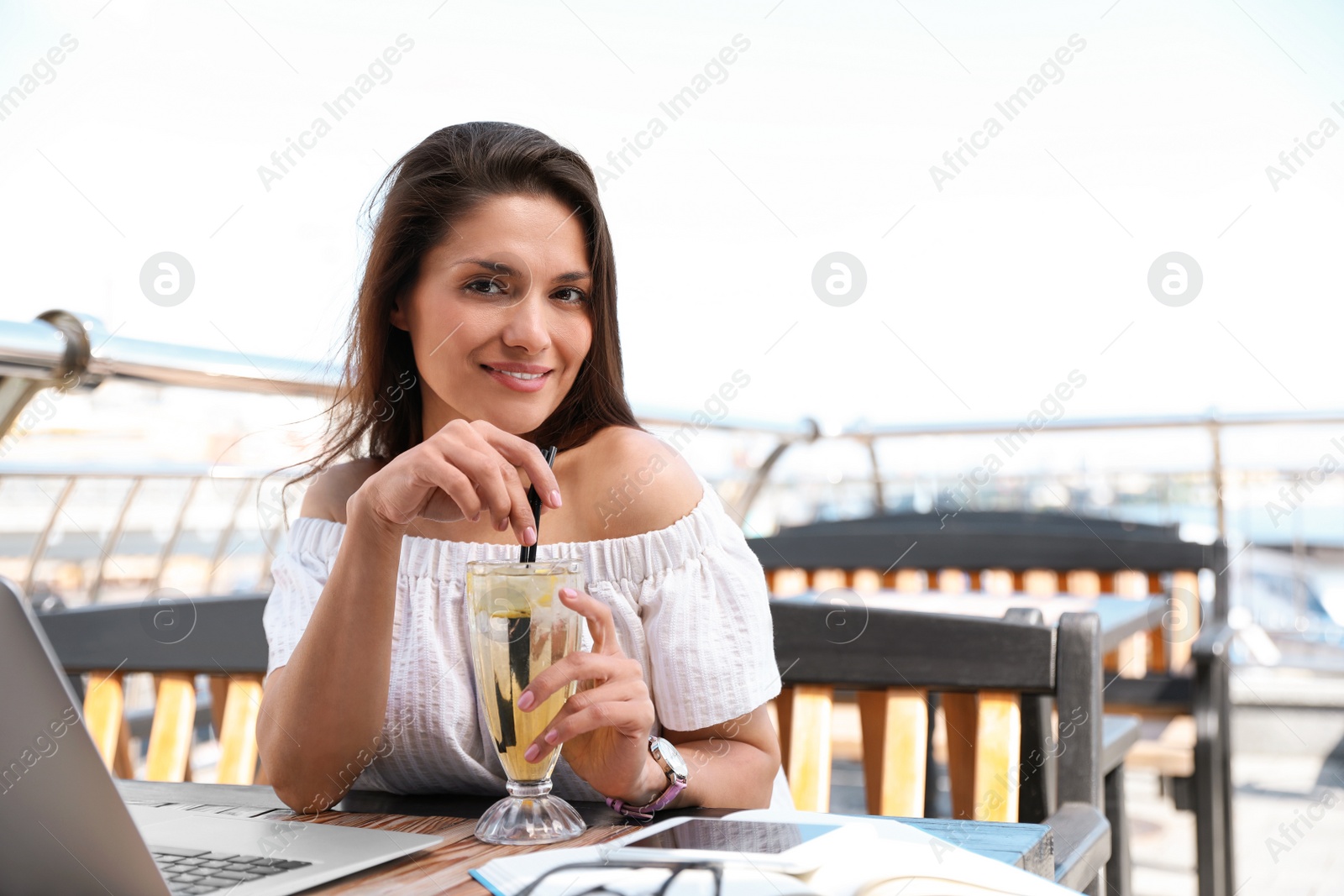 Photo of Beautiful woman with refreshing drink and laptop at outdoor cafe