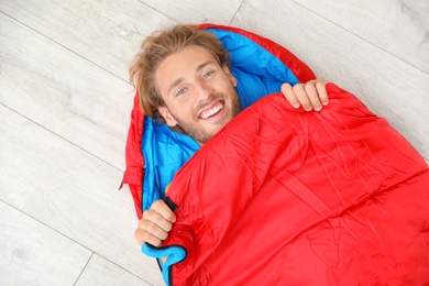 Photo of Young man in comfortable sleeping bag on floor, top view