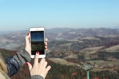 Woman taking photo of beautiful mountain landscape with smartphone