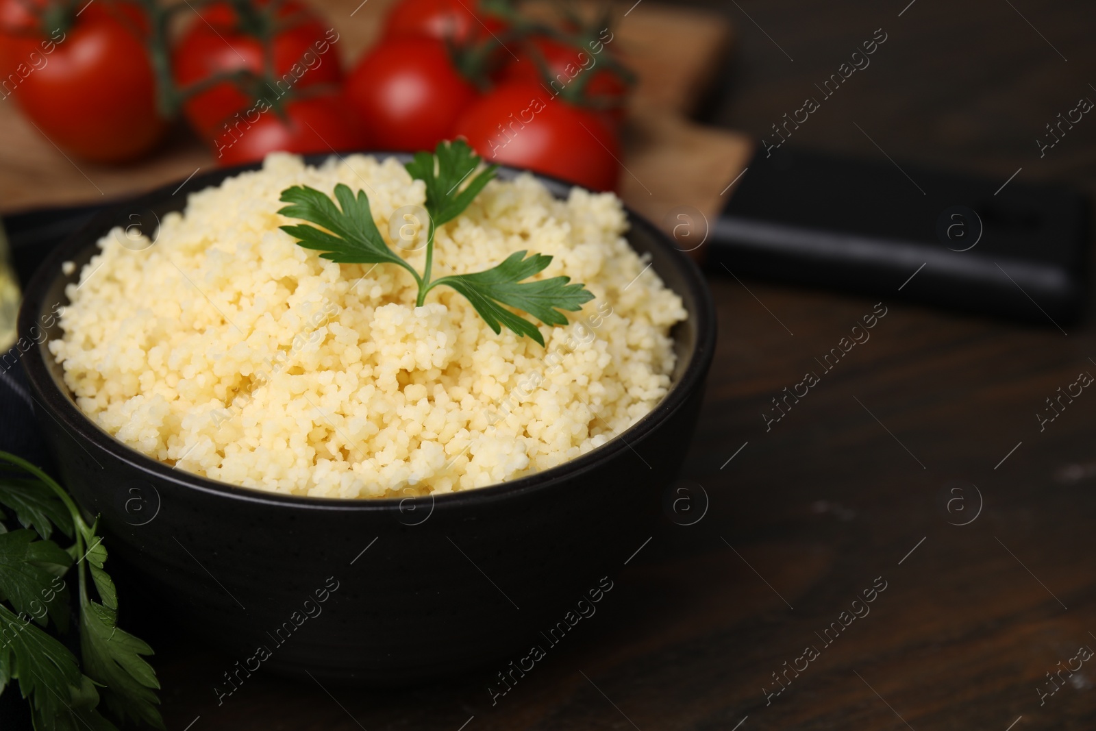 Photo of Tasty couscous and fresh parsley in bowl on wooden table, closeup. Space for text