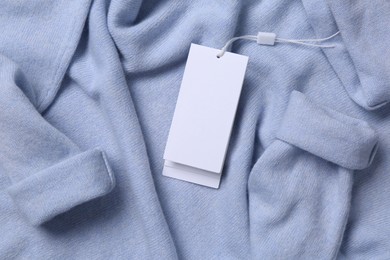 Blank white tags on light blue sweater, top view. Space for text