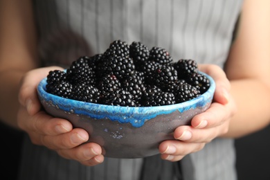 Photo of Young woman holding bowl of ripe blackberries, closeup