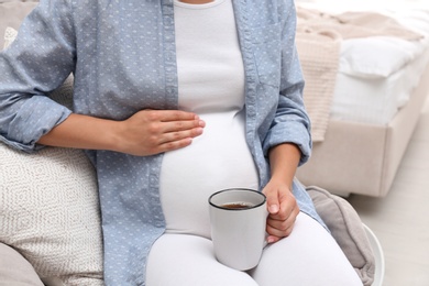 Pregnant woman drinking tea at home, closeup