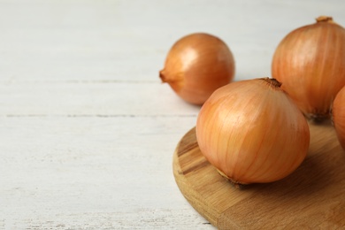Photo of Board with ripe onions on white wooden table, space for text