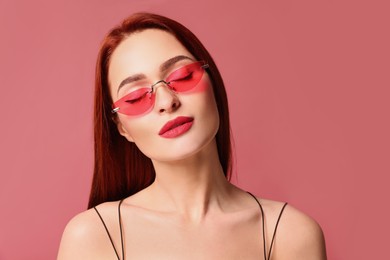 Photo of Beautiful woman with red dyed hair and sunglasses on pink background