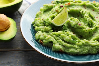 Photo of Delicious guacamole with lime and fresh avocado on grey wooden table, closeup