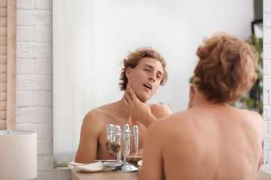 Young man looking in mirror after shaving at home