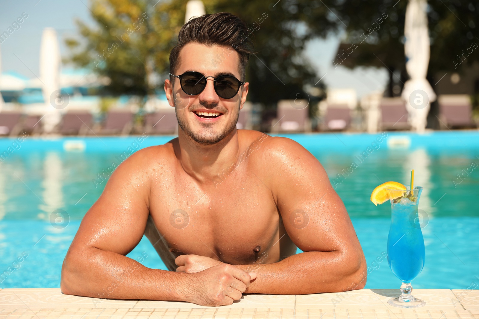 Photo of Young man with cocktail in pool on sunny day