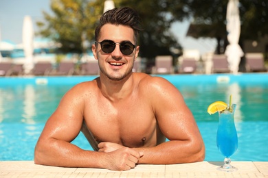 Young man with cocktail in pool on sunny day