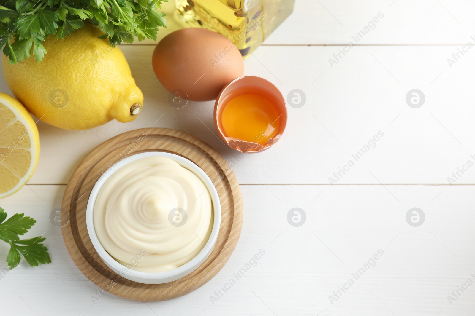 Photo of Fresh mayonnaise sauce in bowl and ingredients on white wooden table, flat lay. Space for text