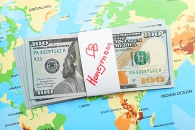 Photo of Stack of money with word Honeymoon on world map, top view