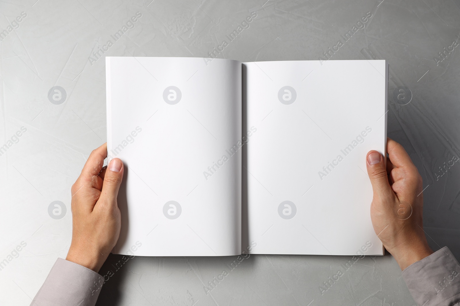 Photo of Man holding blank book at light grey table, top view. Mockup for design