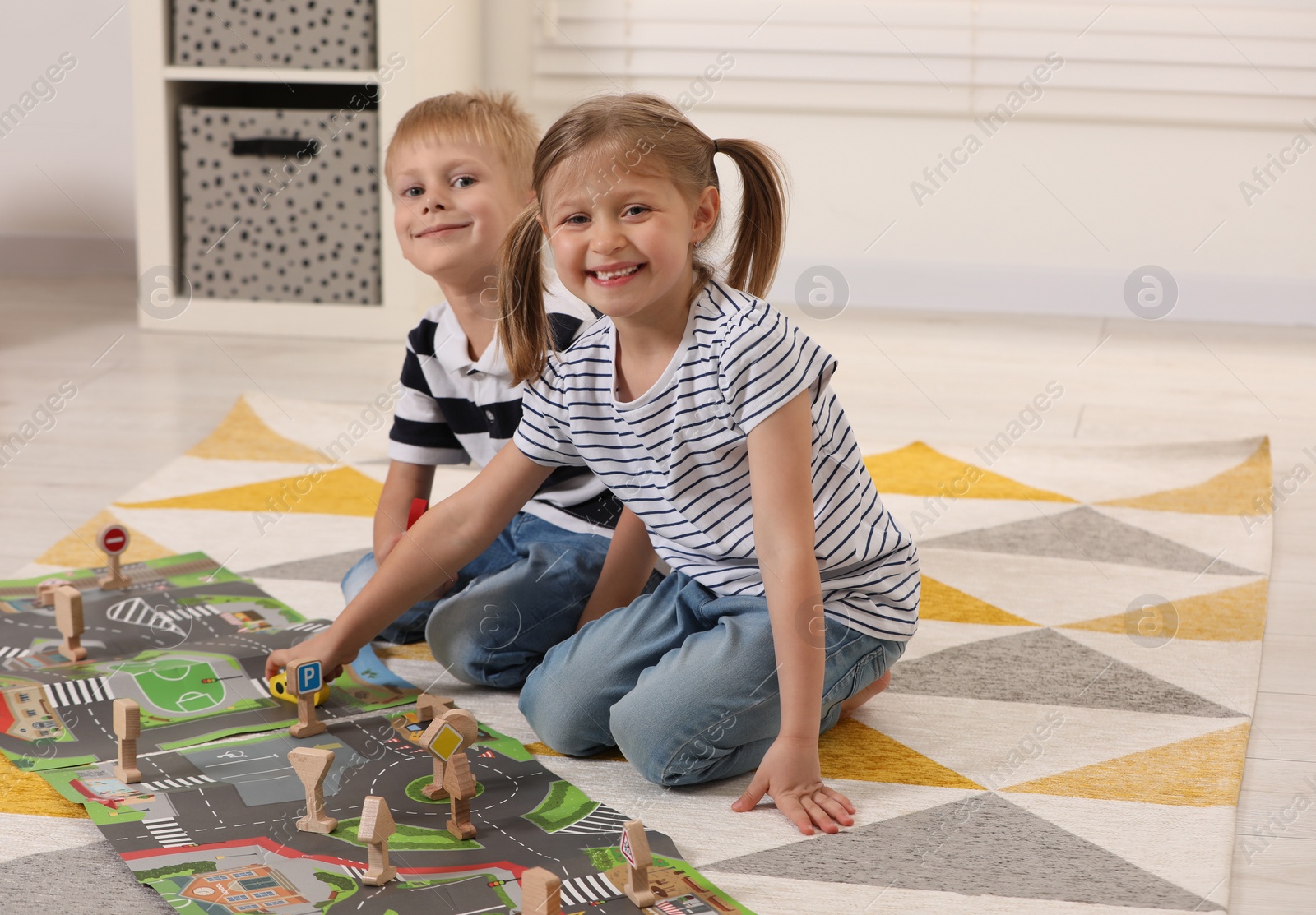 Photo of Little children playing with set of wooden road signs and toy cars indoors