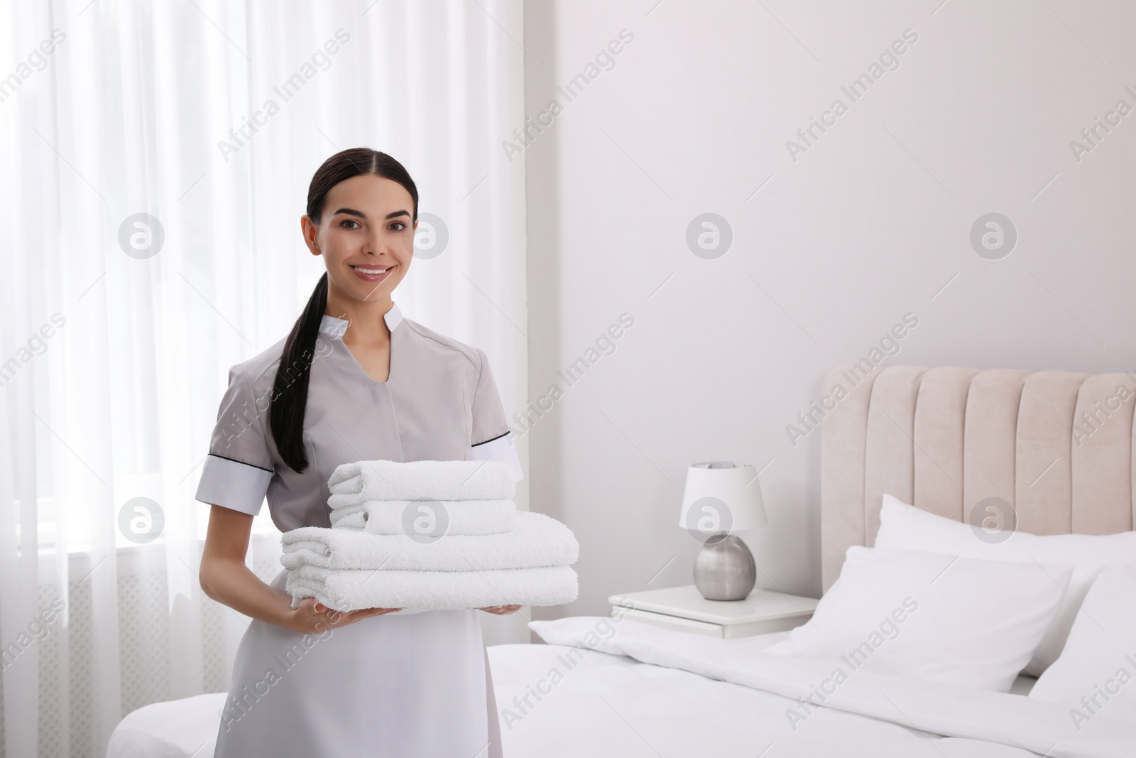 Photo of Chambermaid with stack of fresh towels in hotel room. Space for text