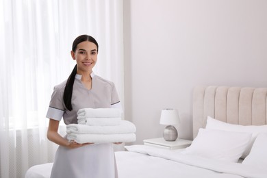 Photo of Chambermaid with stack of fresh towels in hotel room. Space for text
