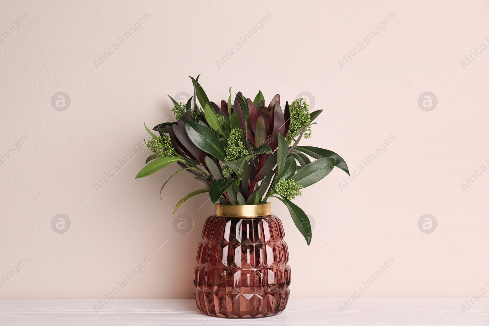 Photo of Vase with beautiful bouquet on white wooden table near beige wall