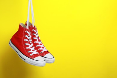 Photo of Pair of new stylish red sneakers hanging on laces against yellow background. Space for text