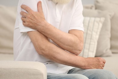 Photo of Senior man suffering from pain in arm on sofa, closeup. Rheumatism symptom