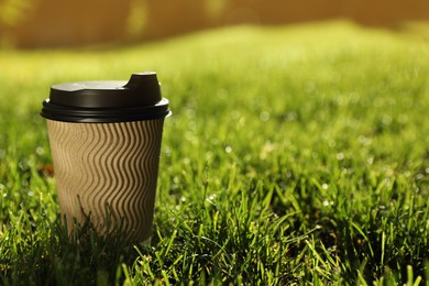 Photo of Cardboard takeaway coffee cup with plastic lid on green grass outdoors, space for text