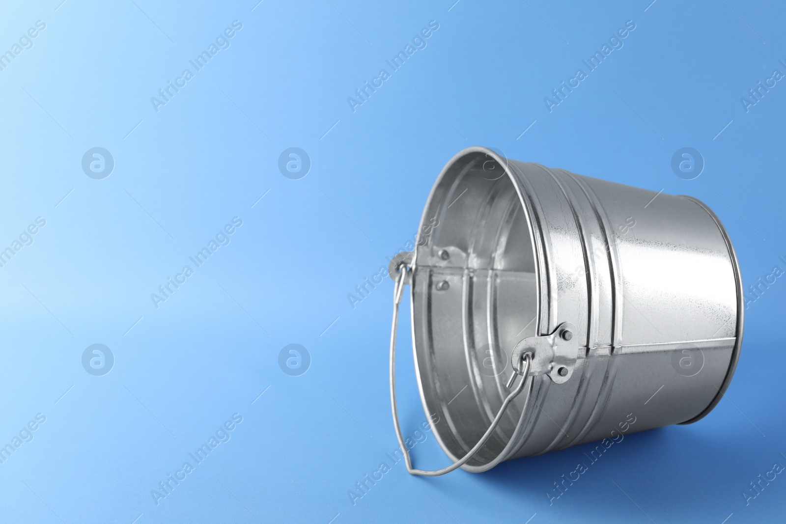 Photo of One shiny metal bucket on light blue background. Space for text