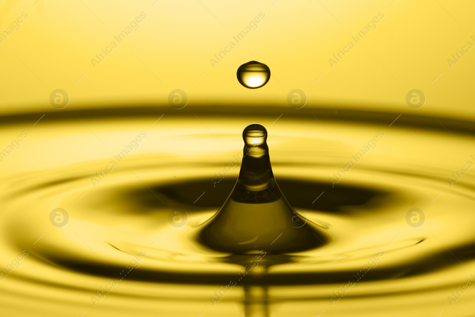 Image of Splash of golden oily liquid with drop on yellow background, closeup