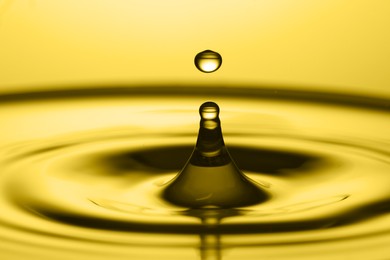 Splash of golden oily liquid with drop on yellow background, closeup