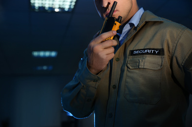 Photo of Professional security guard with portable radio set in dark room, closeup