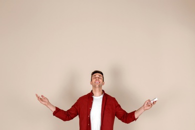 Photo of Young man operating air conditioner with remote control on light background